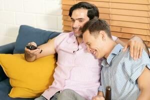 dois homens dentro casual roupas sentado em sofá abraçando e assistindo televisão com Cerveja e pizza dentro vivo quarto às lar. lgbt gay relação conceito. foto