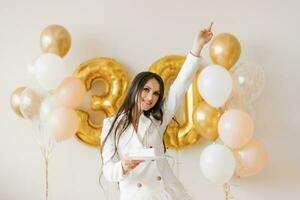 jovem caucasiano mulher segurando uma bolo com uma vela dentro honra do a trigésimo aniversário dentro uma à moda branco vestir com penas foto