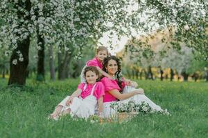 fofa mãe e dois filhas estão tendo uma piquenique dentro a Primavera jardim. ao ar livre atividade. doce momentos família foto