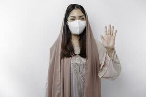jovem ásia muçulmano mulher vestindo uma mascarar e hijab mostra dela Palma ou Pare gesto, cobiçado prevenção conceito foto