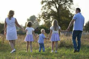 feliz família mãe, pai, crianças, filho e filhas dentro natureza às pôr do sol. pais e crianças estão caminhando junto. a ampla família. foto