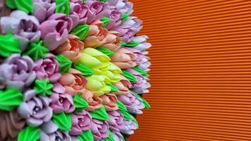 multicolorido creme tulipas em uma bolo em uma fundo do laranja ondulado papel foto