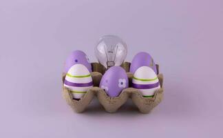 a cartão ovo recipiente contém lilás Páscoa ovos e uma tungstênio luz lâmpada. foto