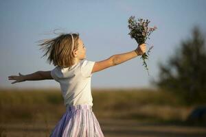 lindo pequeno menina dentro a Prado com uma ramalhete do flores uma criança dentro uma lindo verão campo. foto