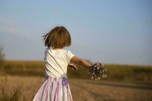 feliz pequeno menina corre em a Prado com uma ramalhete do flores criança em uma lindo verão campo contra a azul céu. foto