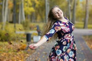 feliz Loiras menina dentro a outono parque dispersa folhas e ri. foto