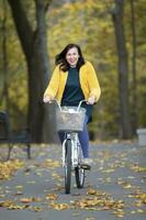 feliz meio envelhecido mulher passeios uma bicicleta dentro a outono parque. foto