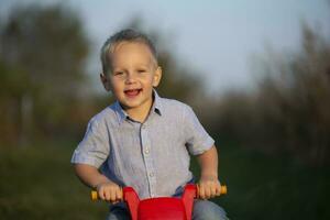 feliz pequeno Garoto é equitação uma vermelho bicicleta e sorridente. foto