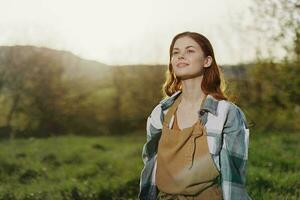 retrato do uma jovem sorridente mulher dentro trabalhos roupas xadrez camisa e avental dentro natureza dentro a tarde depois de trabalhos foto