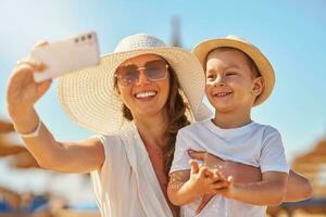 imagem do mãe com filho levando selfie em a de praia foto