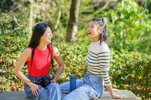 feliz ásia mulheres em repouso durante caminhada viagem dentro floresta foto