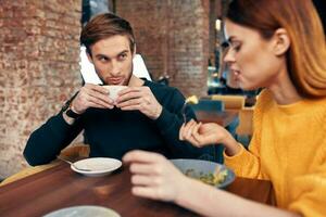 mulher tendo jantar às uma mesa dentro uma cafeteria e uma homem com uma copo do café dentro a fundo foto