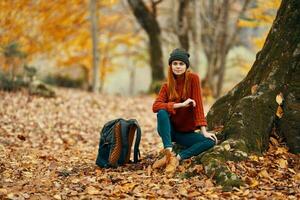 mulher perto árvore e mochila para viagem caído folhas outono floresta foto