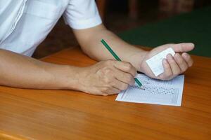 fechar-se aluna fazendo exame, usar lápis para escrever em papel e Veja às respostas em outro mão para enganação a teste. conceito, desonesto comportamento. Educação avaliação. foto