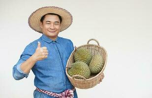 bonito ásia homem agricultor desgasta chapéu, azul camisa, detém cesta do durian frutas, polegares acima. conceito, agricultura ocupação. tailandês agricultores crescer durian frutas Como econômico e exportação frutas Produção foto