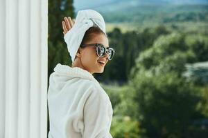 retrato do linda mulher dentro uma branco roupão em a sacada mordeu em verde natureza estilo de vida foto