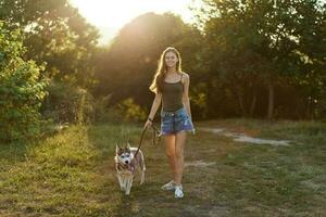 mulher e dela rouco cachorro caminhando alegremente em a Relva dentro a parque sorrir com dentes dentro a outono andar com dela bicho de estimação, viagem com uma cachorro amigo foto