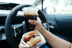 ásia mulher motorista aguarde e comer Hamburger dentro carro, perigoso e risco a acidente. foto