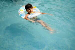 feliz indiano Garoto natação dentro uma piscina, criança vestindo natação traje ao longo com ar tubo durante quente verão Férias, crianças Garoto dentro grande natação piscina. foto