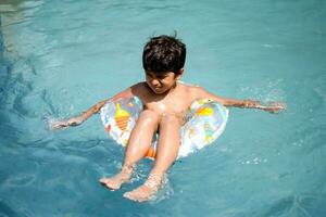 feliz indiano Garoto natação dentro uma piscina, criança vestindo natação traje ao longo com ar tubo durante quente verão Férias, crianças Garoto dentro grande natação piscina. foto