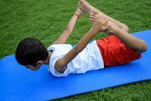 ásia inteligente criança fazendo ioga pose dentro a sociedade parque ar livre, crianças ioga pose. a pequeno Garoto fazendo ioga e meditação exercício. foto