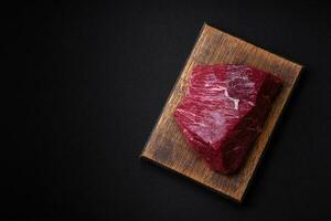 uma peça do fresco cru carne com sal, especiarias e ervas em uma de madeira corte borda foto