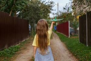 menina criança feliz com longos cabelos loiros brincando com avião de brinquedo ao ar livre ao pôr do sol foto