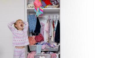 pequeno menina dentro Rosa Rosa pijamas trava coisas dentro a armário, bagunça dentro a quarto foto