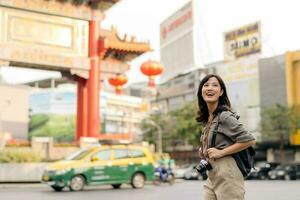 jovem ásia mulher mochila viajante desfrutando China Cidade rua Comida mercado dentro Bangkok, tailândia. viajante verificação Fora lado ruas. foto