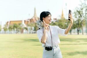 retrato lindo jovem ásia mulher com Smartphone em verão feriado período de férias viagem com a grande Palácio dentro uma fundo às Bangkok, Tailândia foto