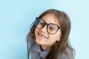 alegre menina de 7 anos de óculos com um sorriso sobre fundo azul. educação infantil, conceito de aprendizagem foto