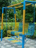 crianças jogar instalações dentro a jardim. azul e amarelo ferro balanço foto