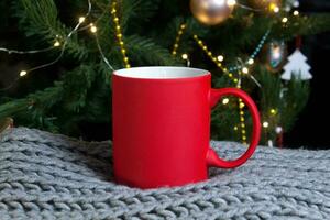 em branco vermelho caneca com Natal árvore em fundo, tapete chá ou café copo com Natal e Novo ano decoração, vertical zombar acima com cerâmico caneca para quente bebidas, vazias presente impressão modelo. foto