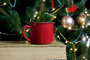 em branco vermelho caneca com Natal árvore em fundo, chá ou café copo com Natal e Novo ano decoração, vertical zombar acima com cerâmico caneca para quente bebidas, vazias presente impressão modelo. foto