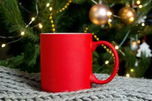 em branco vermelho caneca com Natal árvore em fundo, tapete chá ou café copo com Natal e Novo ano decoração, vertical zombar acima com cerâmico caneca para quente bebidas, vazias presente impressão modelo. foto