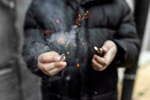 a fogo de artifício dentro uma mão. Garoto segurando uma queimando petardo dentro dele mão. criança com uma pirotecnia este queimaduras com faíscas e fumaça ao ar livre. fogo de artifício e isqueiro dentro mão. foto