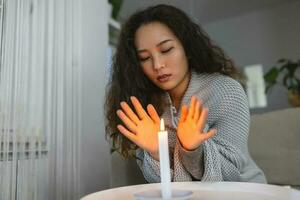 queimando vela, mulheres tentando para calor dela mãos dentro Sombrio lar. desligar do aquecimento e eletricidade, poder interrupção, queda de energia, carga derramamento ou energia crise foto