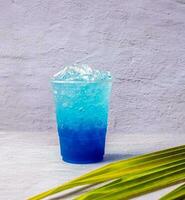 bebida havaiana azul em um copo de plástico e folhas de coco. foto