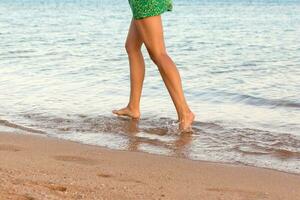perna do mulher corrida em de praia com água espirrando. verão período de férias. pernas do uma menina caminhando dentro água em pôr do sol foto