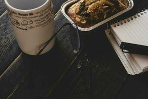 banana bolo em uma Preto de madeira mesa com Nota livro, copos, e café canecas. foto