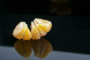 laranja fresco suculento tangerina fatias em a fundo do lustroso Preto vidro fechar-se foto