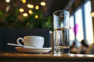 uma branco copo do café e uma vidro do água em uma mesa dentro uma cafeteria foto