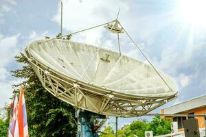 grande satélite prato às televisão estação debaixo brilhante azul céu e Sol flare fundo. foto