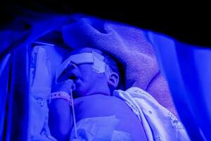 fechar-se doente recém-nascido bebê dormindo em bebê cama com ultravioleta luzes do fototerapia unidade para tratamento neonatal hiperbilirrubinemia foto