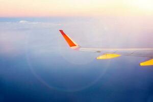 lado de fora janela Visão do avião com aeronave asa com lente clarão, Sol flare e céu do pôr do sol fundo. foto