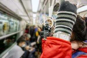 mão dentro fio luva segurando lidar com ciclo dentro uma metrô em embaçado pessoas fundo. foto