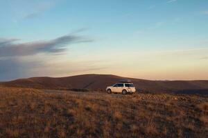 branco carro suv estacionado perto cênico rota estrada dentro outono Cáucaso panorama. natural Cáucaso ponto de referência e popular destinos. bagagem tronco caixa montanhoso em carro cobertura prateleira. foto