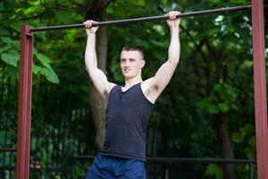 Forte homem fazendo pull-ups em uma Barra ao ar livre foto