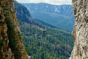 uma pessoa passagem uma através da ferrata ponte rota entre dois falésias. Esportes vida dentro a montanhas. ativo vida. alpinista usando apropriado equipamento para segurança. através da ferrata sokolov colocar romanija dentro bih. foto