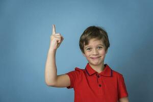 uma fofa caucasiano Garoto do 5 anos velho dentro uma vermelho camiseta afirmativamente e alegremente pontos dele dedo acima foto